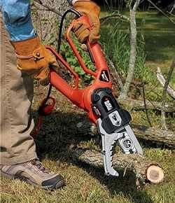 Man with heavy leather gloves using a smallish chain saw to cut tree branches laying on grass.