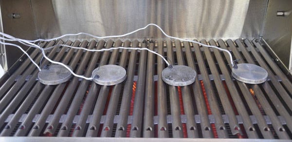 A shiny steel rack with glowing red flame underneath. Shiny metal disks hooked to thin, white cable rest on the rack.