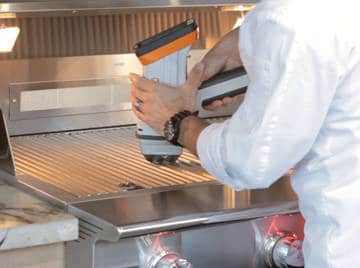 Manin white jacket holds a large plastic tool over a shiny, stainless steel surface.