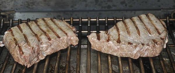 Two thick steaks cooking on a bbq grill.