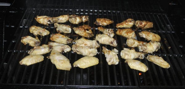 Chicken wings cooking on a bbq grill. The ones at the front of the grill are raw while those at the back are cooked.